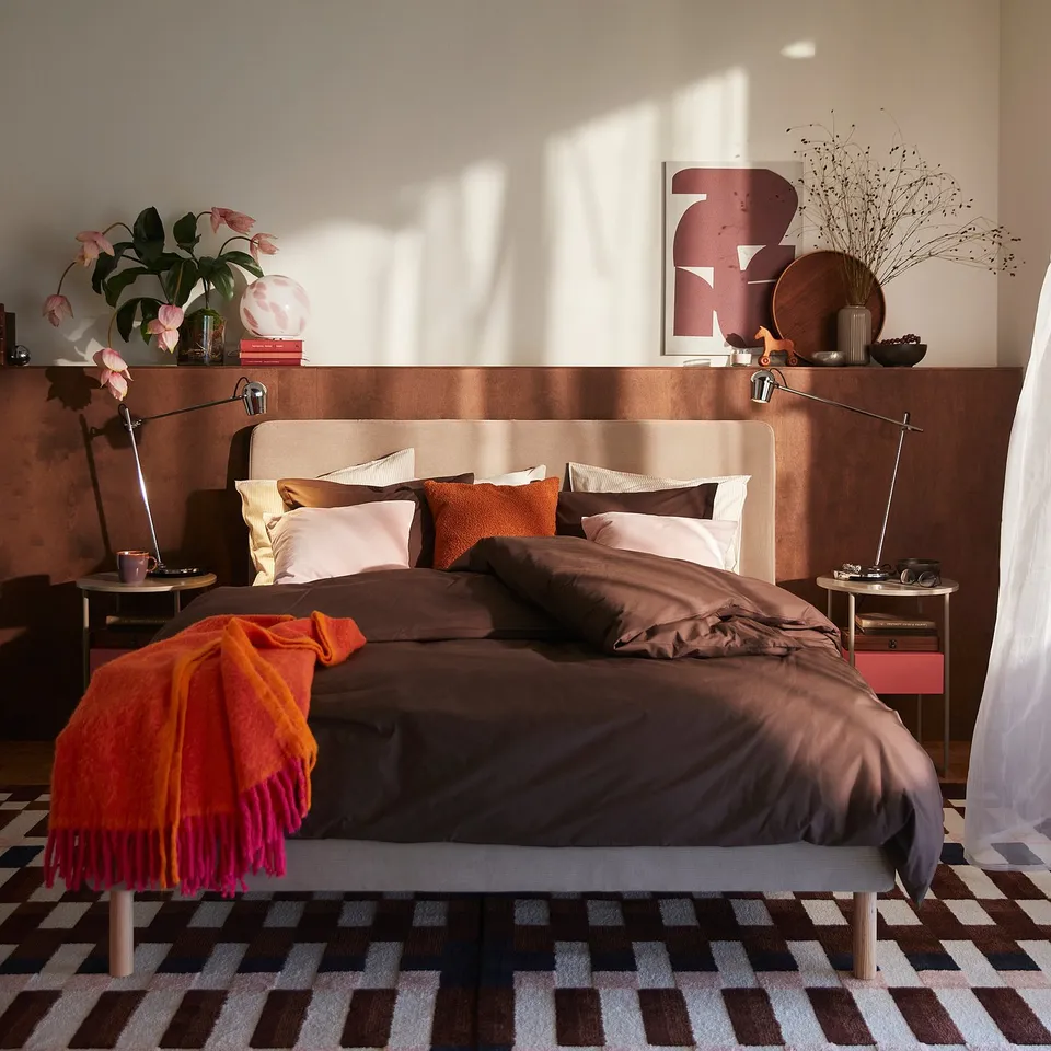 Brown cotton duvet set on large bed with pillows, colourful rug, art, and lamps.