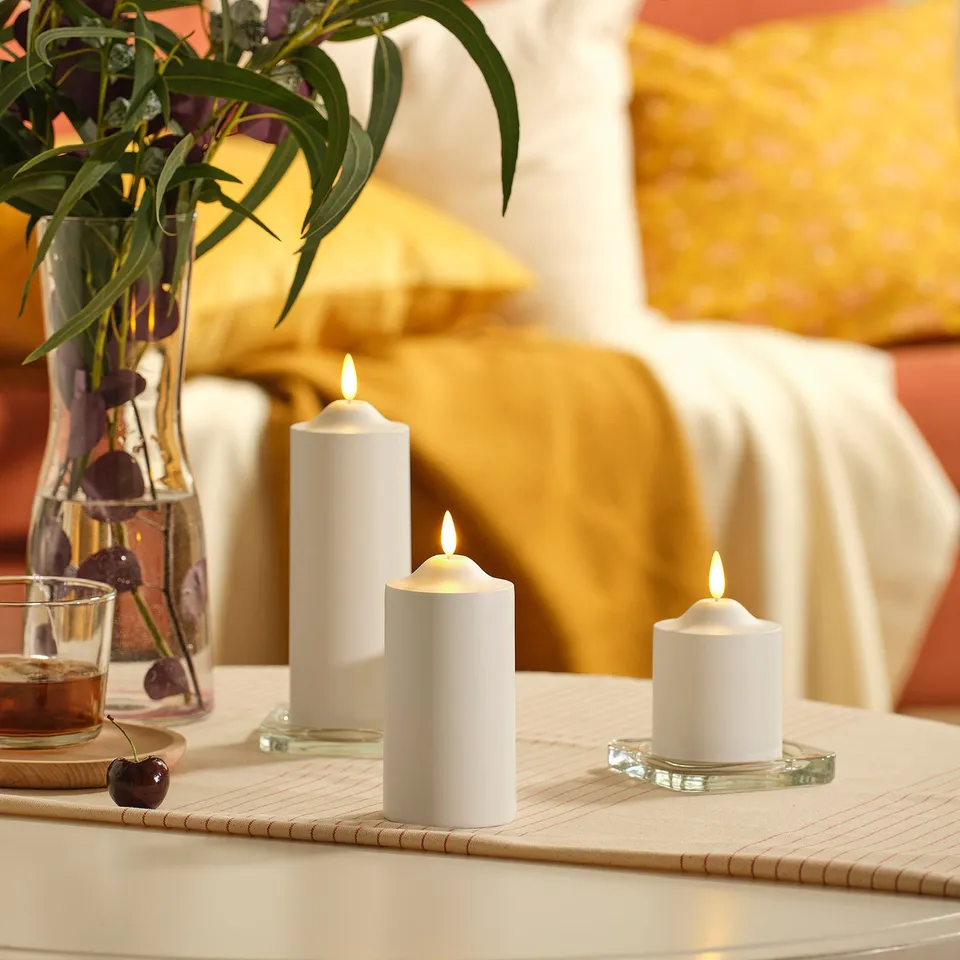 Three SMÅLOM led candles on cream runner, vase of flowers, cherry in glass.
