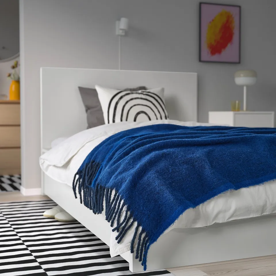 Modern bedroom with white bed, blue throw, grey pillows & abstract art.