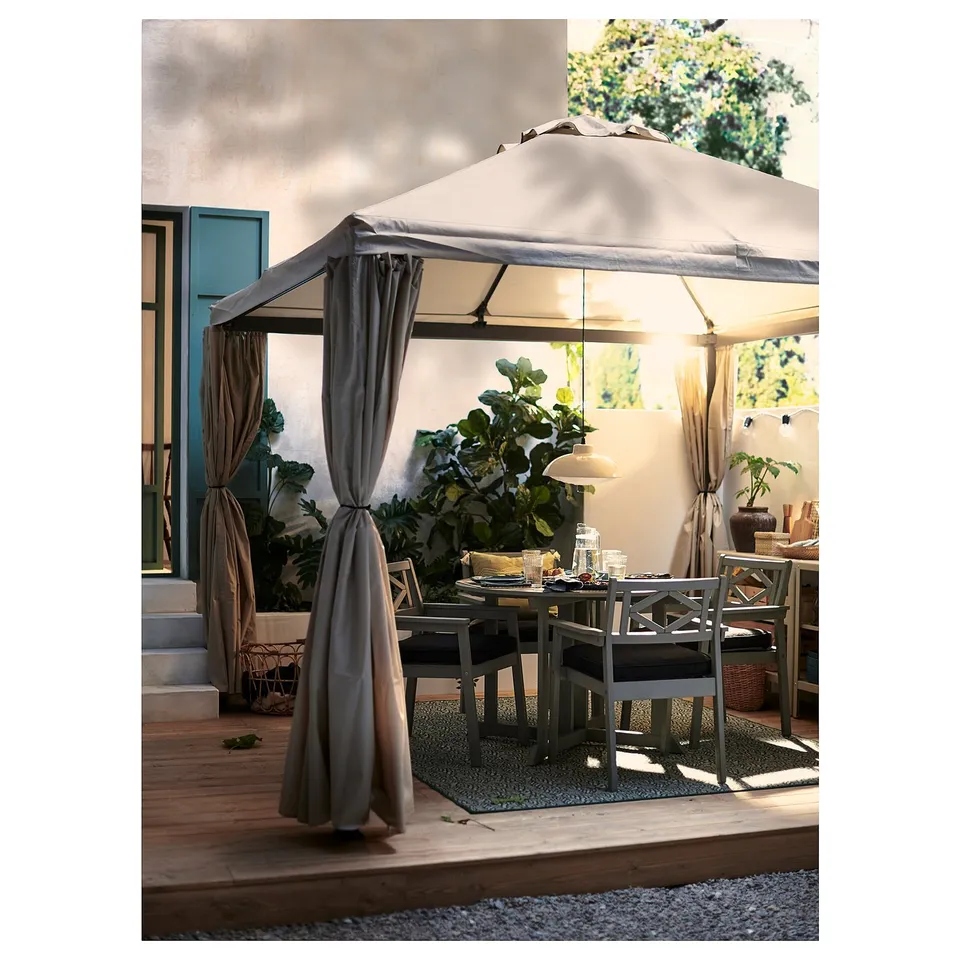 Cosy outdoor gazebo with beige curtains and table set on a terrace.
