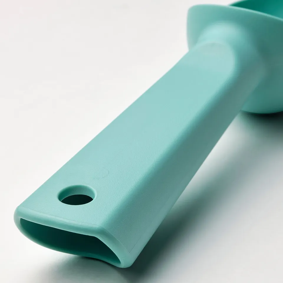 Turquoise plastic ice-cream scoop, smooth surface with hole, resting on light blue background.