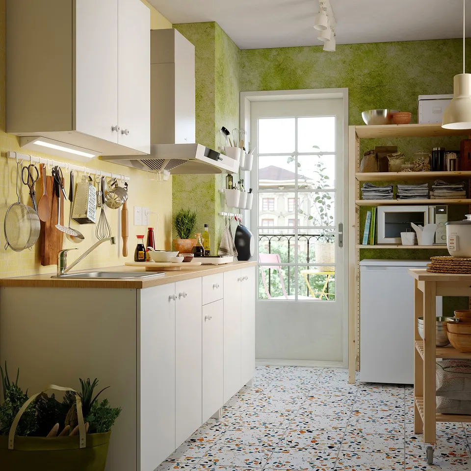 Well-organized kitchen with white cabinets, wooden countertop, green walls, and patterned floor. Refrigerator, shelves, and hanging utensils visible.