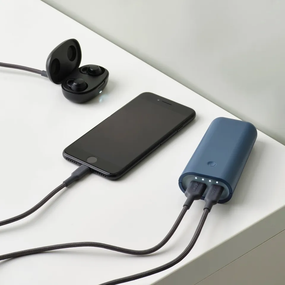 Smartphone and earbuds charging simultaneously via portable power bank with dual usb ports.