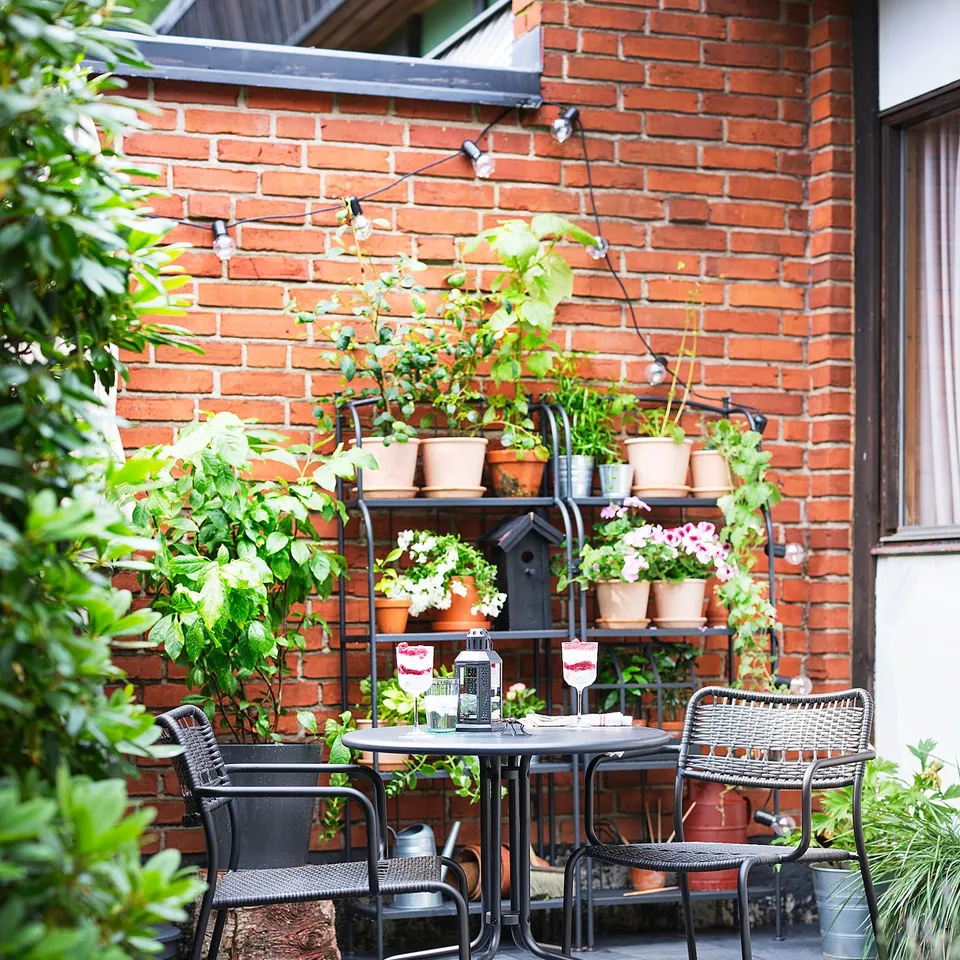 Small, black, wrought-iron patio set against brick wall with plants.