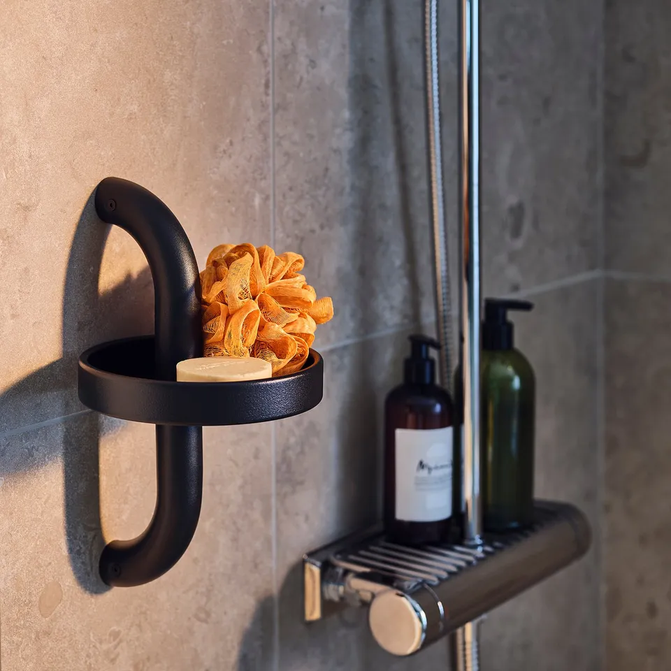 Black shower handle shelf set. Includes orange bath sponge and two soap dispensers mounted on grey tiled wall.