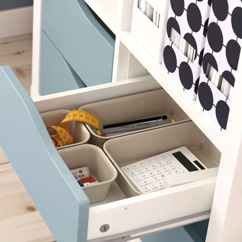 A KALLAX organiser with storage drawers. Drawers hold a tape measure, calculator, pens, and small containers with items.