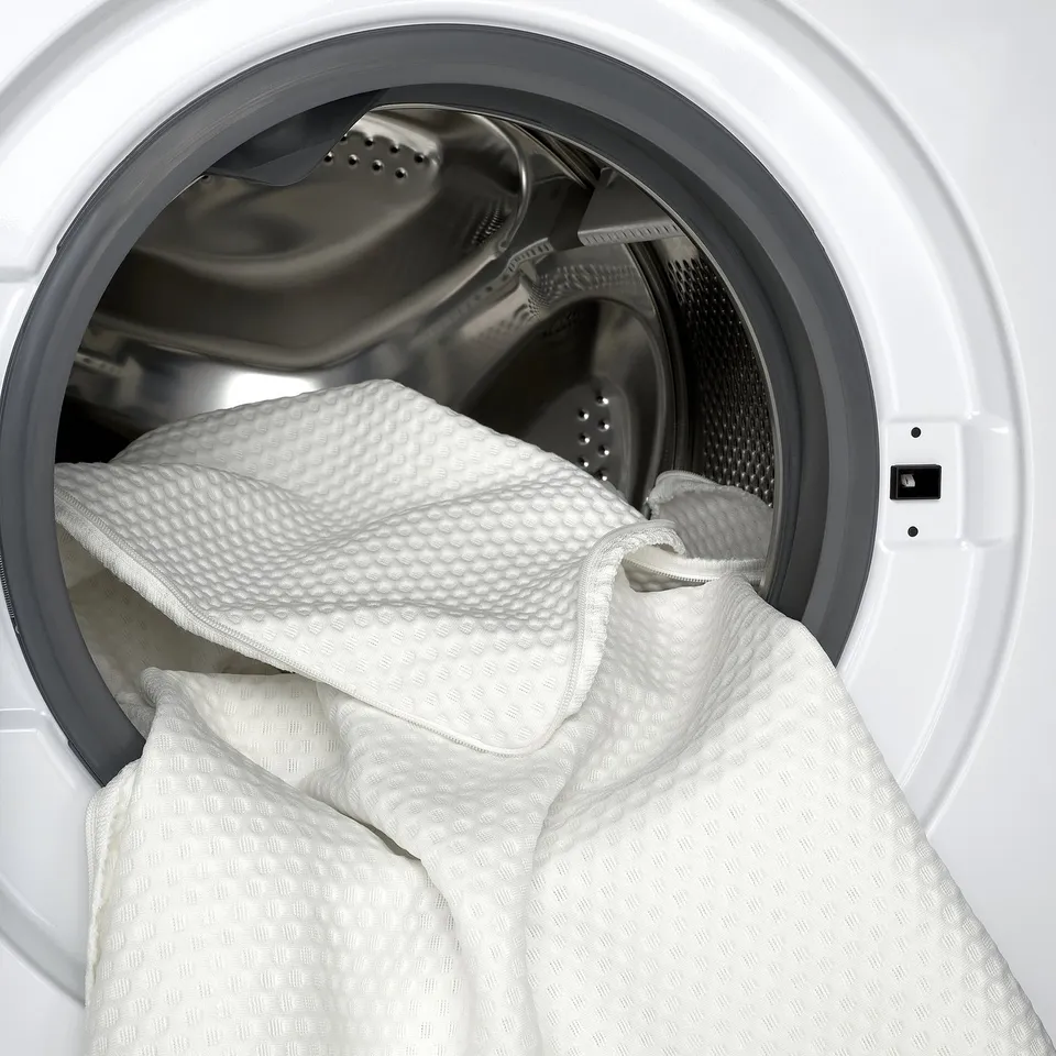 White mattress pad with memory foam inside washing machine, highlighting its washable cover for easy cleaning and maintenance.