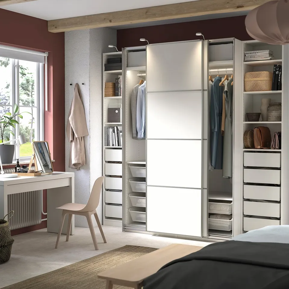 Modern bedroom with PAX wardrobe, sliding doors, hanging clothes, shelves, and a desk with chair.