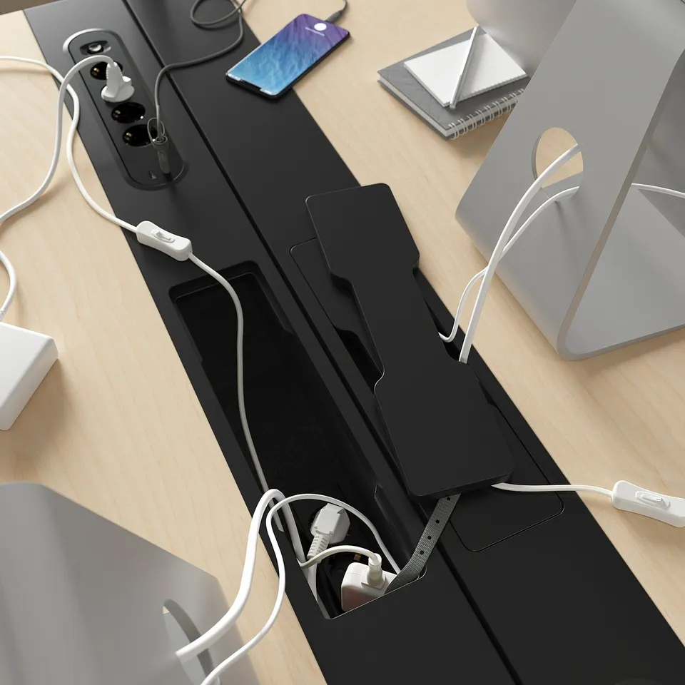Black desk with power sockets, cord management, charging devices. Smartphone, notebook, and monitor setup.