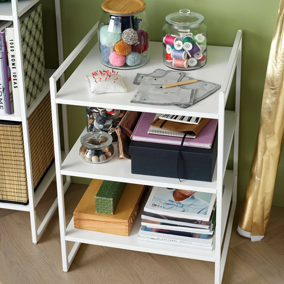 White three-tier JONAXEL storage shelf, holding diy supplies, notebooks, and magazines. The metal frame and shelves are neatly organised.