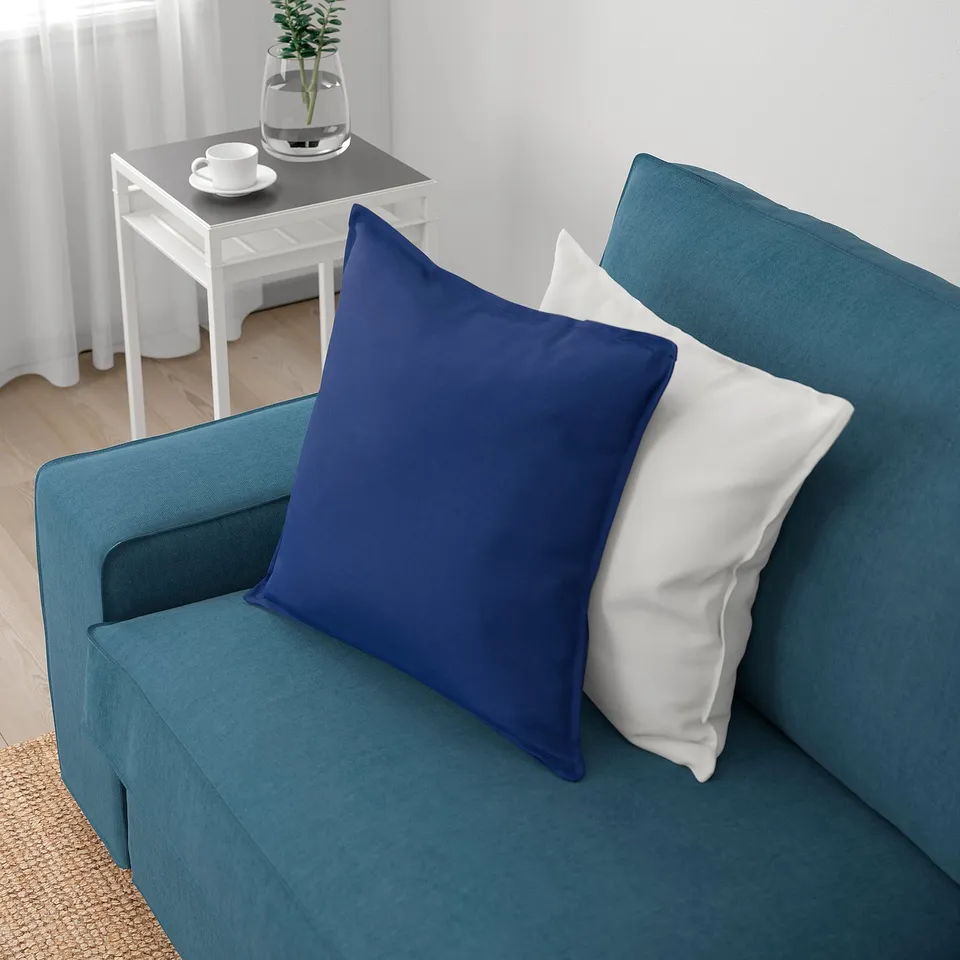 Blue sofa with two pillows, one white, one navy. White side table with plant and cups beside.