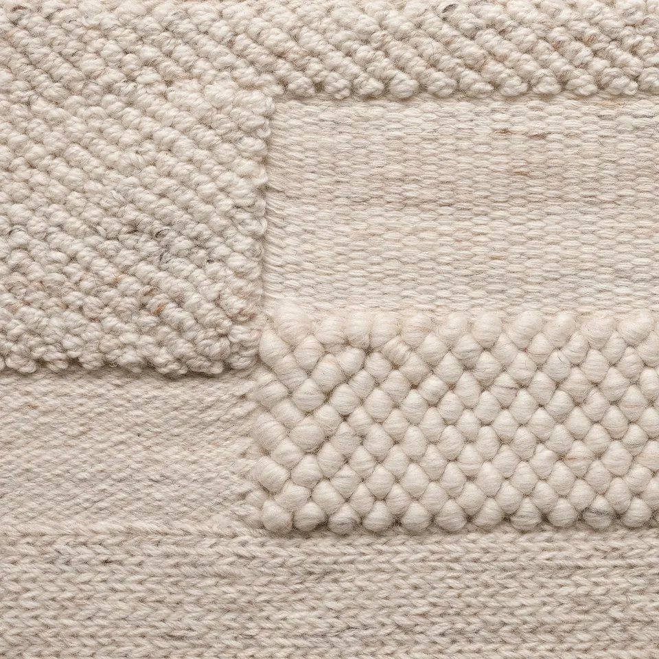 Close-up of woven wool rug, showcasing intricate textures and neutral tones.