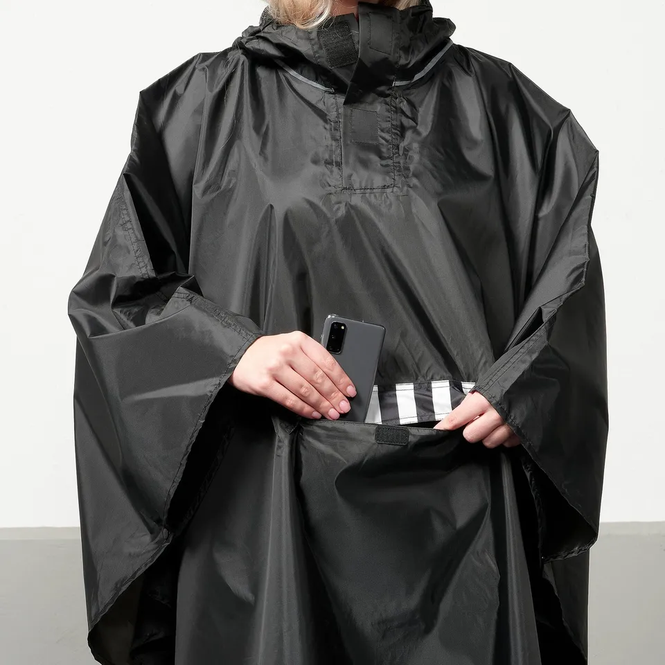 Person wearing black SALTSTEN poncho holding phone in front pocket.