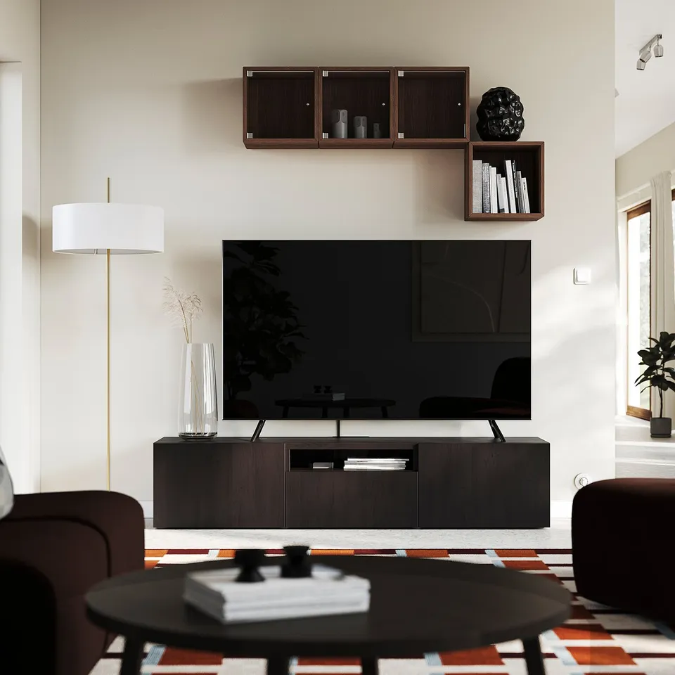 Modern living room with BESTÅ tv unit. Dark wood, large flat screen, shelves with decor, soft lighting. Brown leather seats, rug, coffee table.
