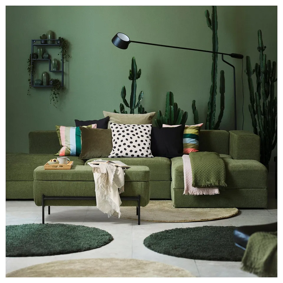 A modern green textured sectional couch with colourful pillows, a plush rug, and a cactus wall mural.