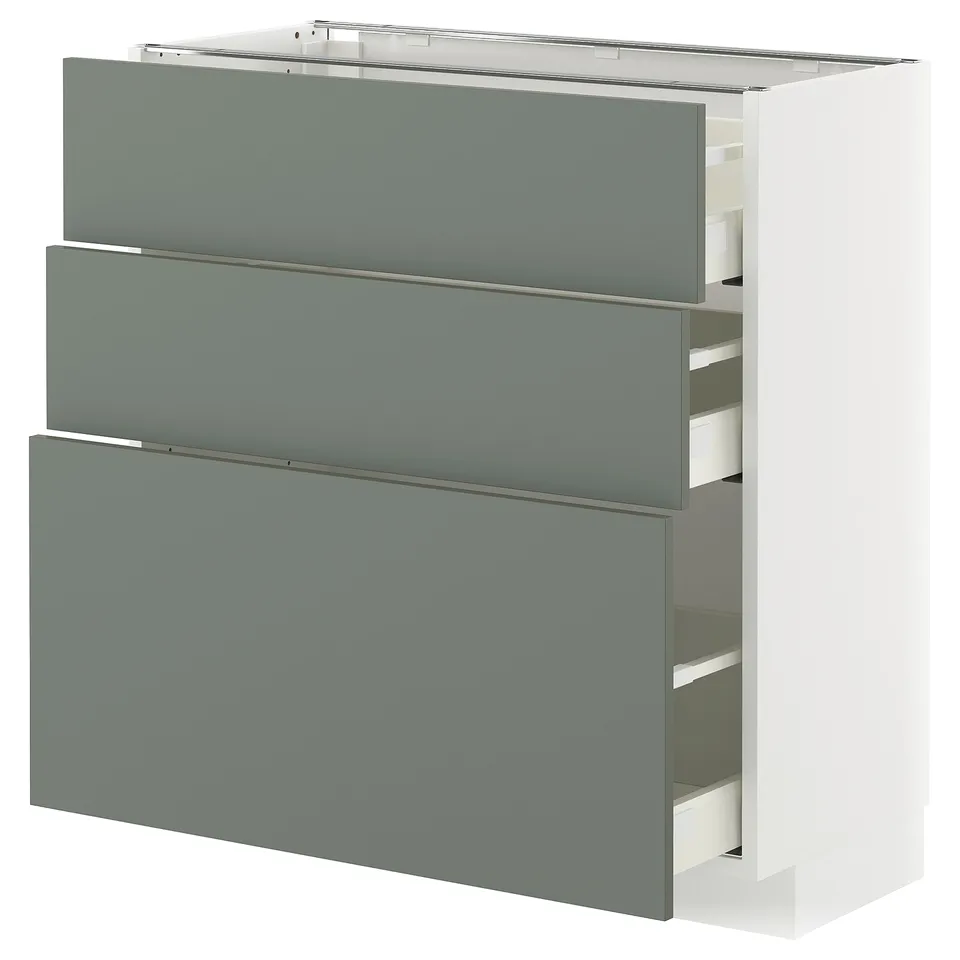 A modern kitchen cabinet called METOD with three grey-green drawers and a white base.