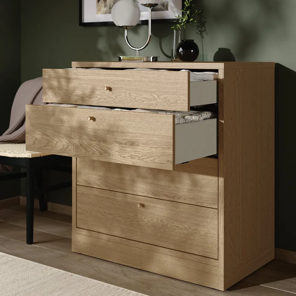 Wooden dressing unit with three open drawers, showcasing soft-close feature. Top: lamp, vases. Bed: visible behind.