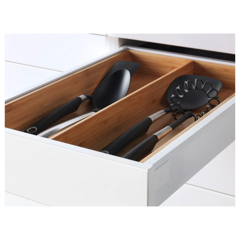Open kitchen drawer showing wooden compartments and black utensils.