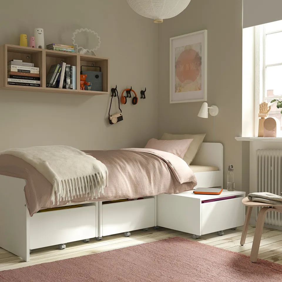 Cosy bedroom with pale pink STOENSE rug, low-pile bed, white drawers, wooden table, and bookshelf with magic poster.