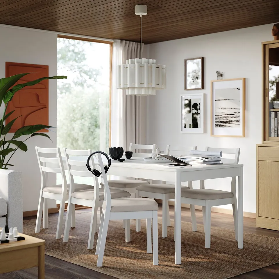 White dining table with 6 matching chairs, melamine top, wooden legs. Cushioned seats, cosy setup.