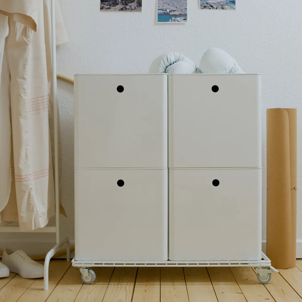 White KUGGIS storage box on wheels near coat rack and rug.