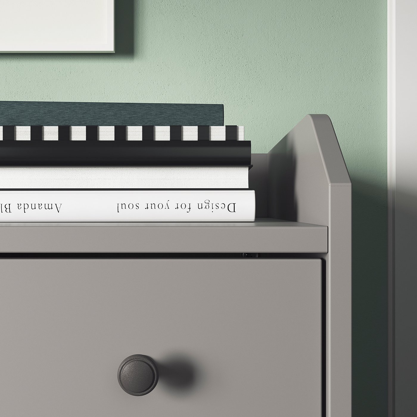 A minimalist grey chest with black knobs and two white books on top.