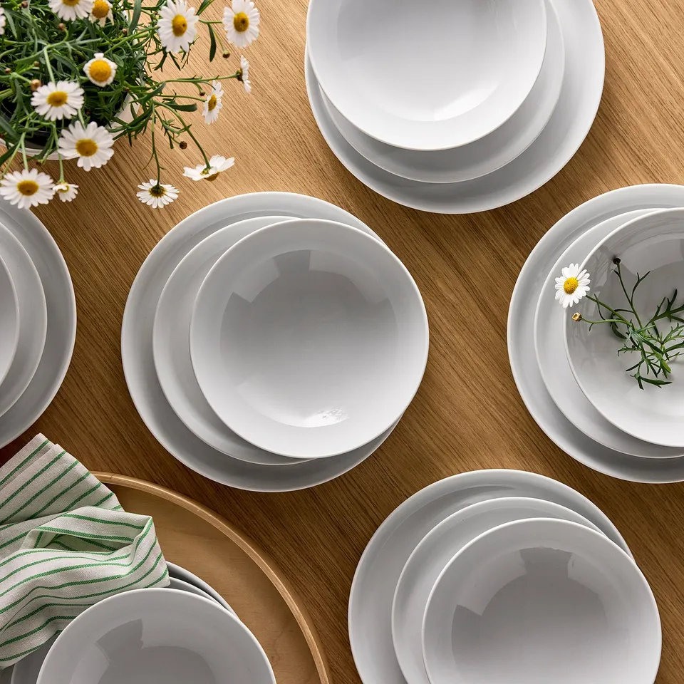 White IKEA 365+ porcelain tableware. Includes plates, bowls, and flowers. Set arranged neatly, ideal for dining.