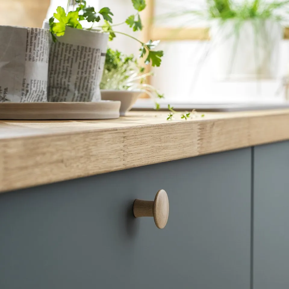 Blue kitchen cabinets with wooden knobs; one round, one oval. Light wooden countertop with pots and plants.