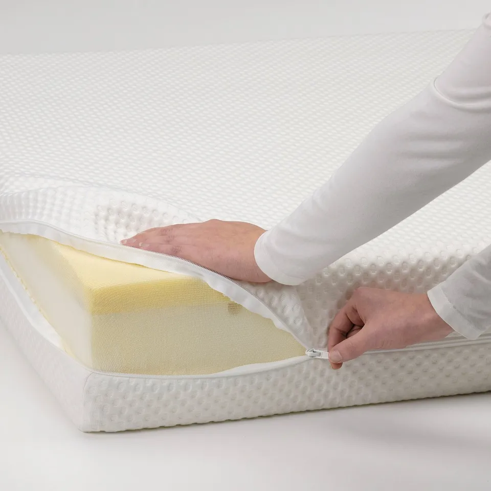 A person adjusting a zip on a white bed mattress, revealing the foam layers inside.