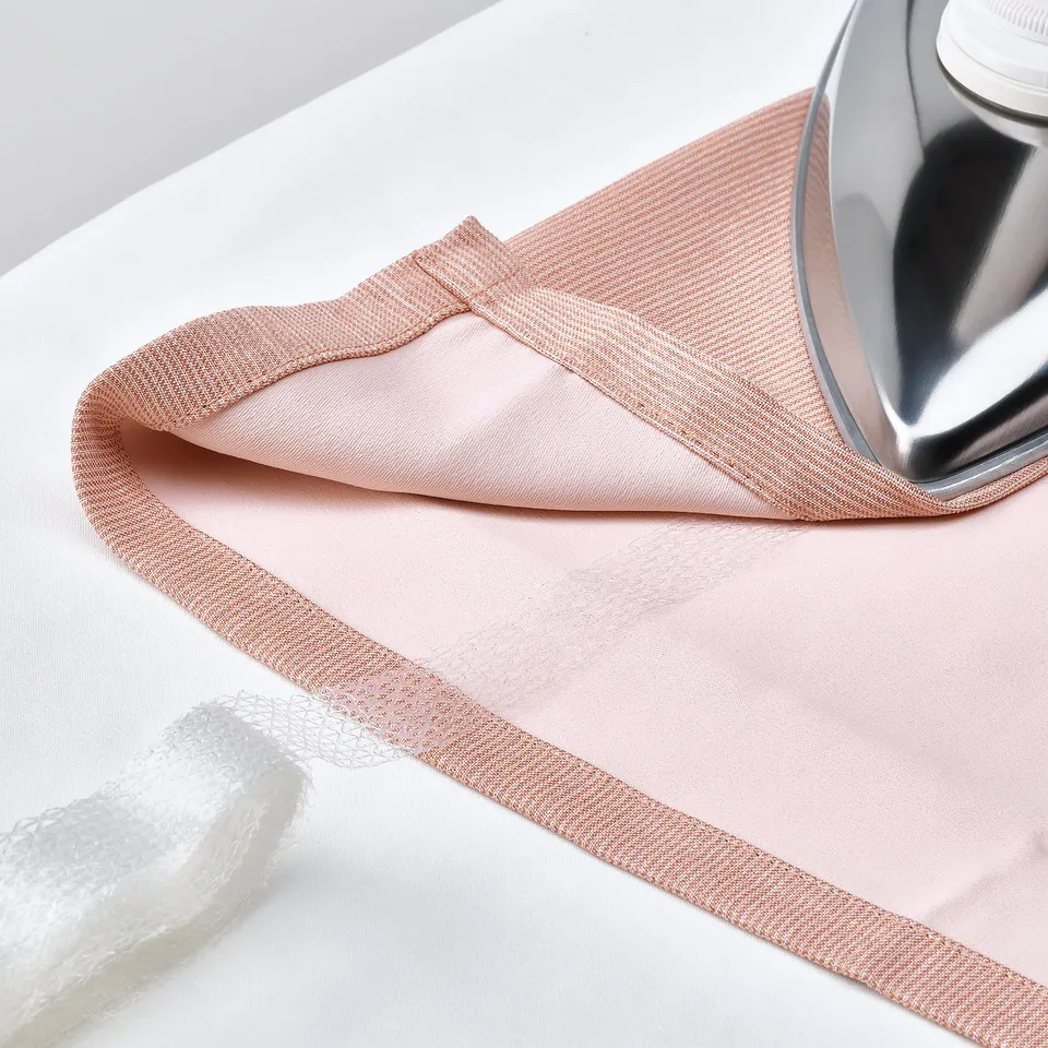 An iron pressing a pink curtain with a textured edge. The curtain has a room-darkening ability and a durable, easy-care fabric.