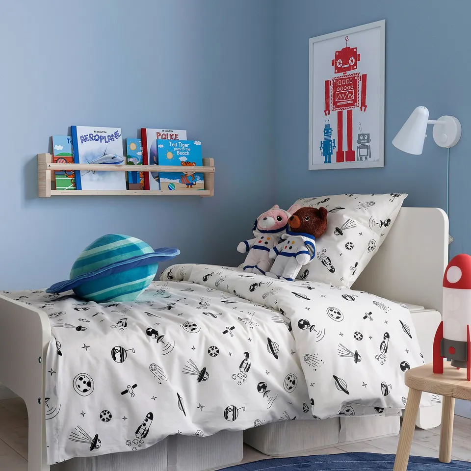 Kids room with blue walls, white bed, space theme. AFTONSPARV duvet, books, robot poster, lamp, cuddly toy.