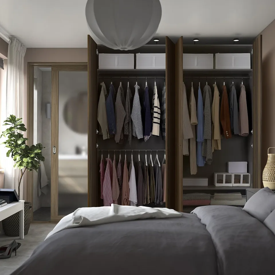 Modern bedroom with a grey bedspread, open wardrobe displaying clothes, and a potted plant by a window.