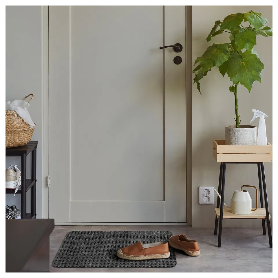 Indoor space with grey chequered FRIKTION mat, shoe cabinet, plant, bench, and cleaning tools.
