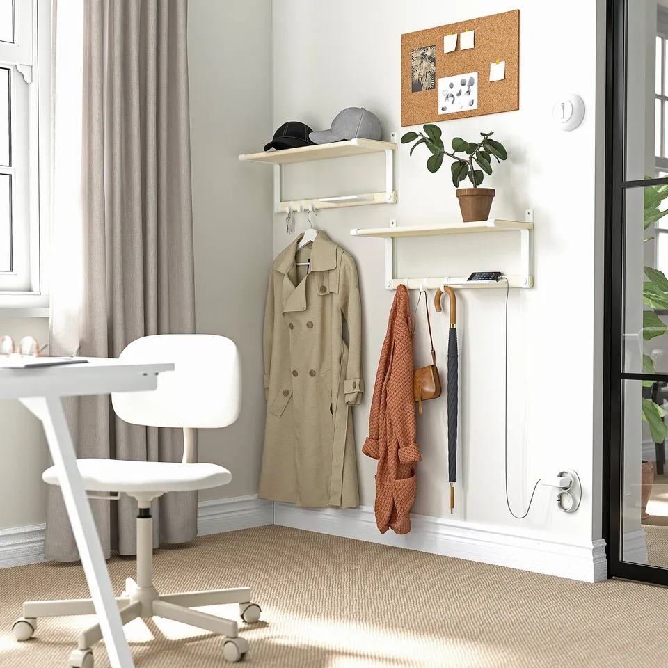 Home area with SKOMAKARE shelf in white. Shelf holds coats, hat, bag, and plant. Desk and chair nearby. Shelf small compared to wall.