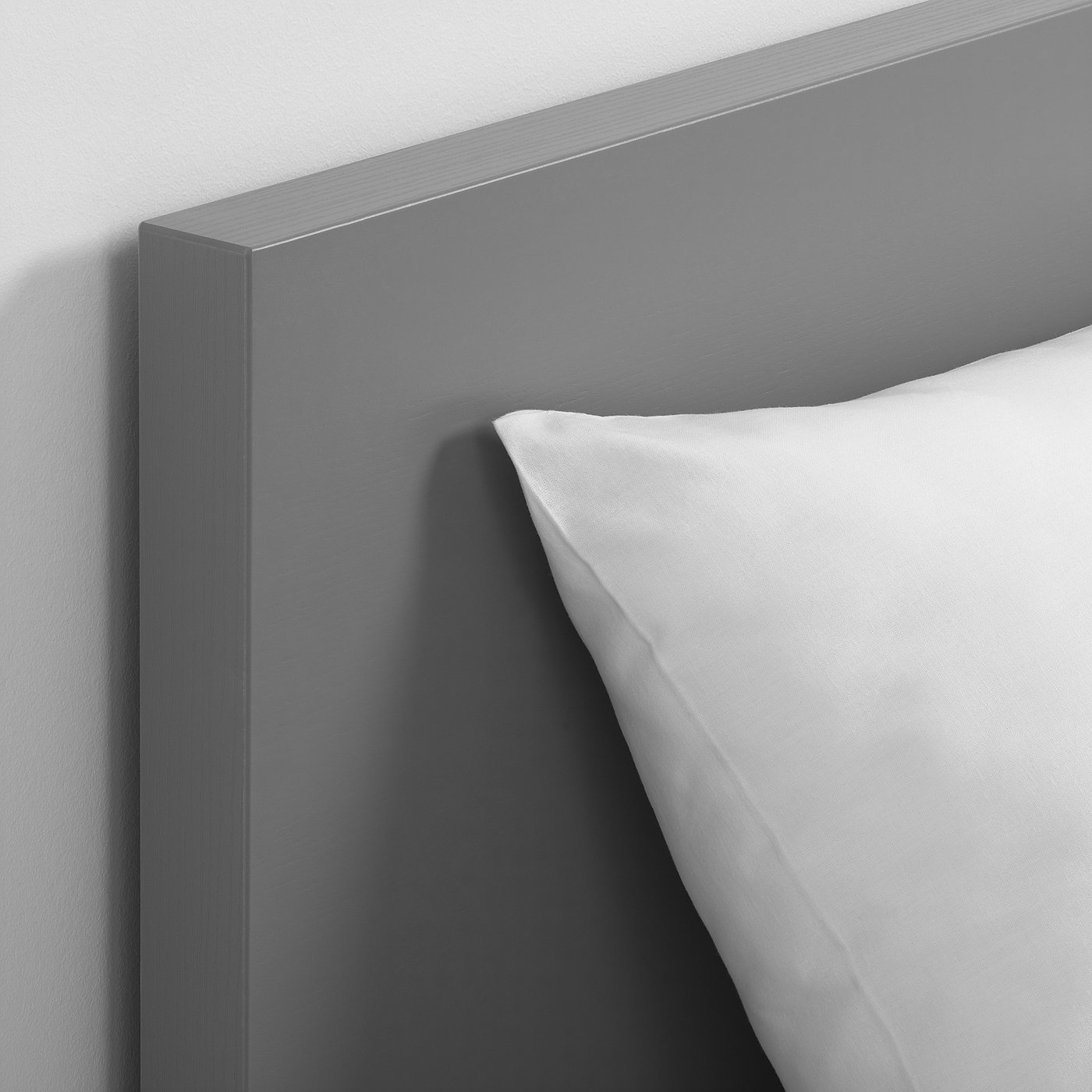 A corner of a modern, grey bed frame with a crisp white pillow, emphasising its sleek and minimalist design.