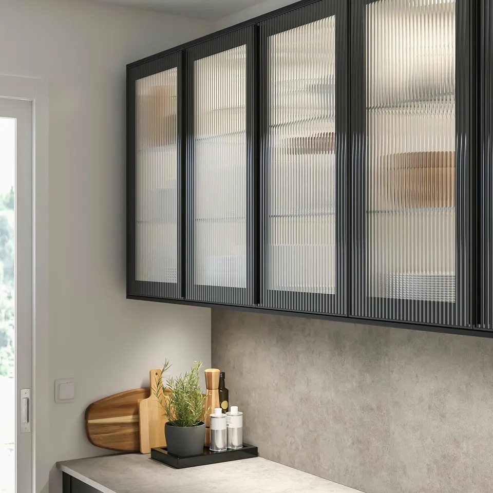 Modern black kitchen cabinets with frosted glass doors, sleek design. Below, counter with wooden cutting board and plant.