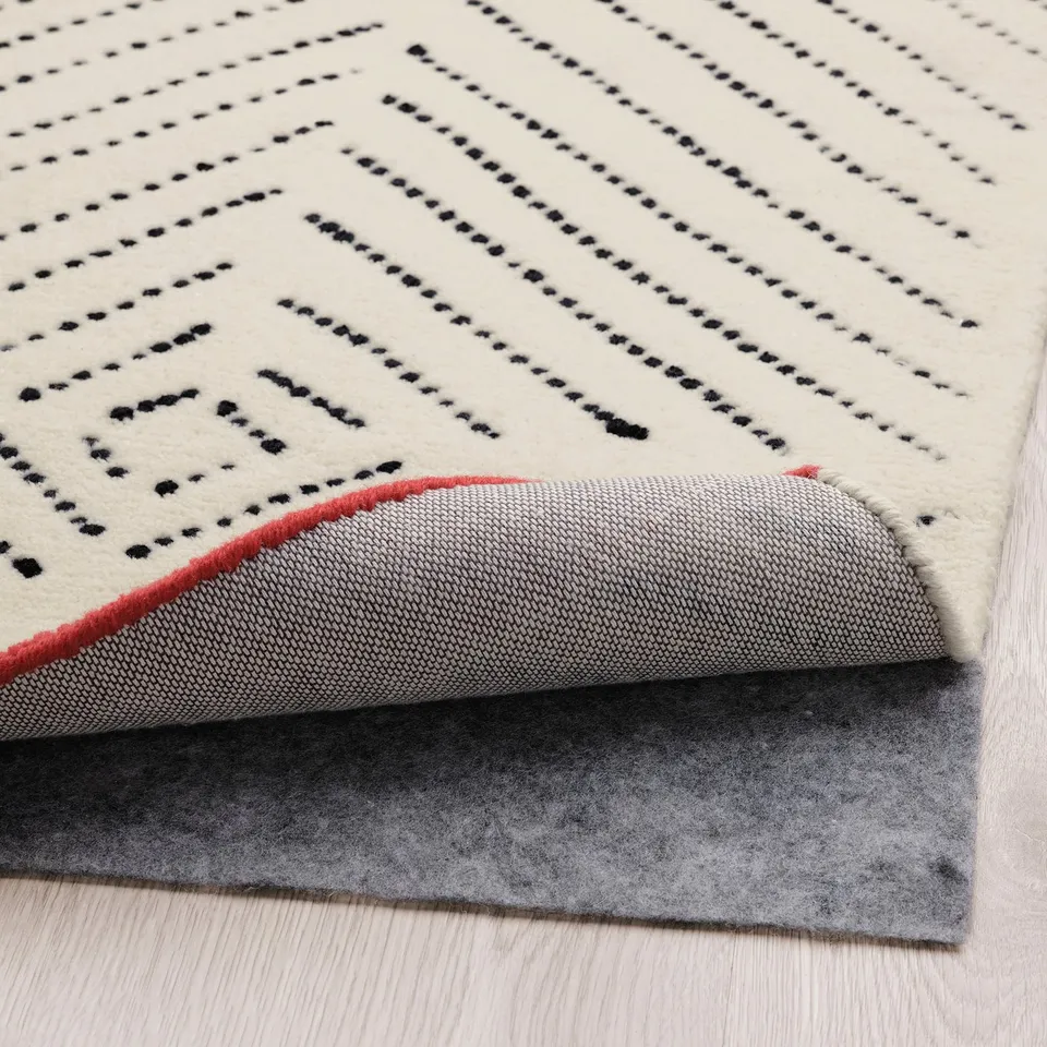 Hand-tufted wool rug with diamond pattern and red edge over grey rug underlay, soft and sound-dampening.