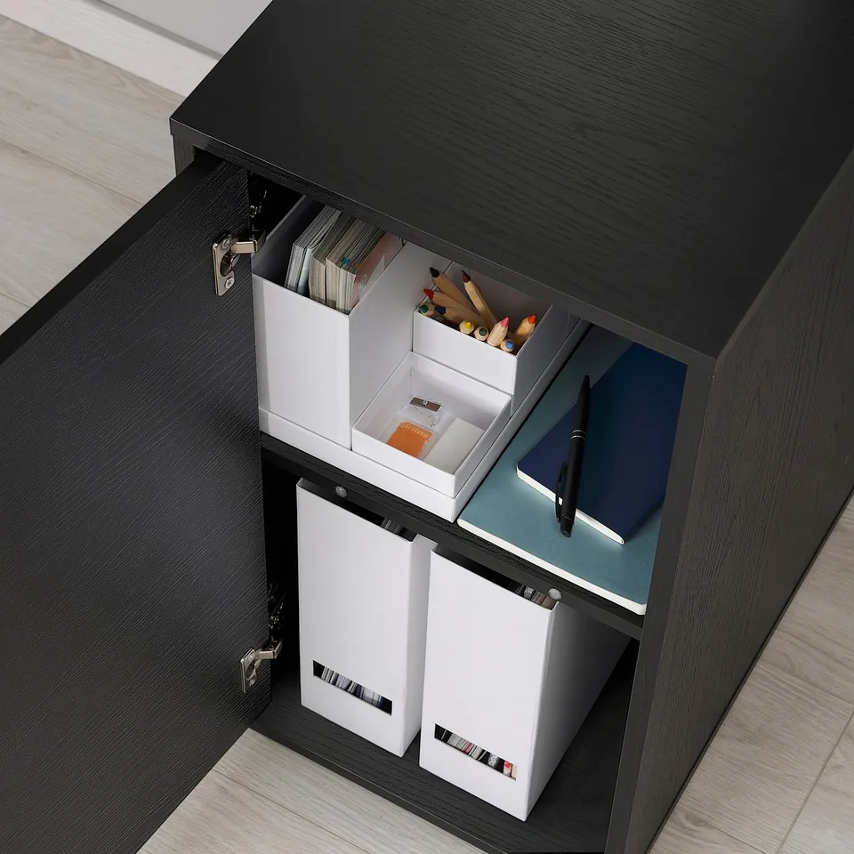 Black cabinet with open door revealing white organisers holding files, office supplies, and a notebook.