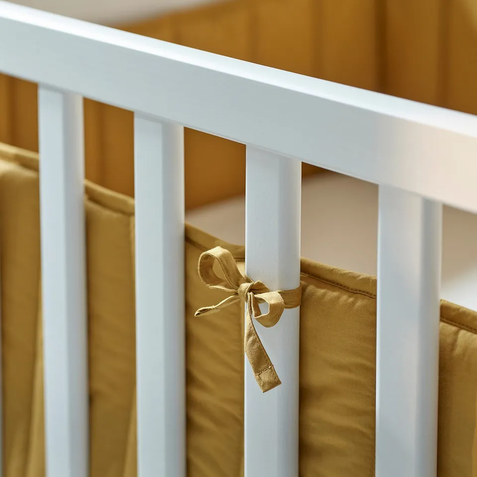 Close-up of a cribs padded bumper tied with decorative ribbons for safety and comfort.