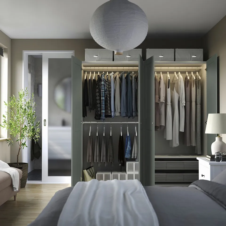 Modern bedroom with open wardrobe displaying clothes, ties, drawers, and a stylish lamp, showcasing organised storage and lighting.