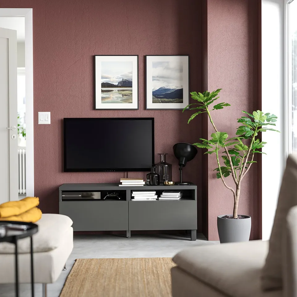 Modern living room with maroon wall, white sofa, grey tv stand, flat screen tv, decorative items, and two framed mountain photos.