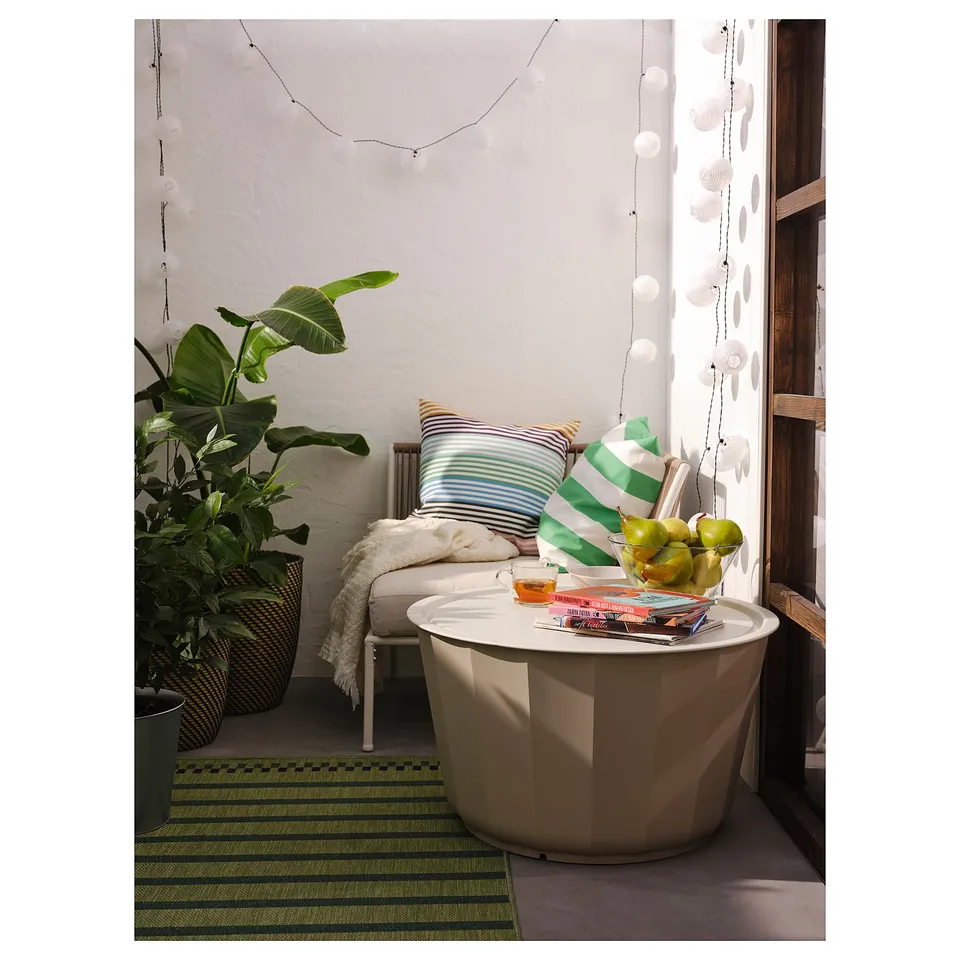 Modern outdoor space with white LÅGASKÄR coffee table, striped cushions, green rug, large plant, and hanging lights.