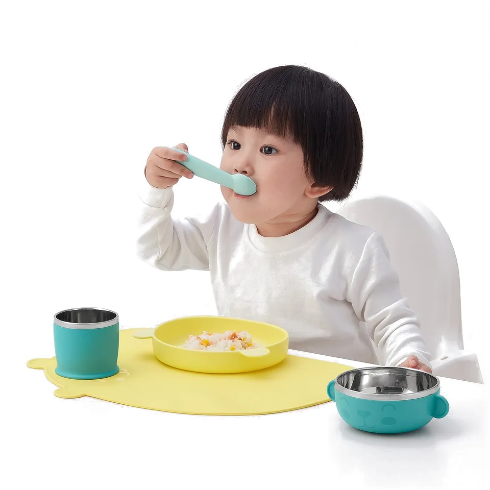 A toddler eating from a yellow bowl on a colourful, non-slip placemat. The placemat has a high edge to contain spills.