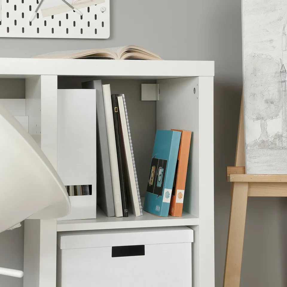 White KALLAX shelf with assorted books and binders, including a teal binder and an orange book.