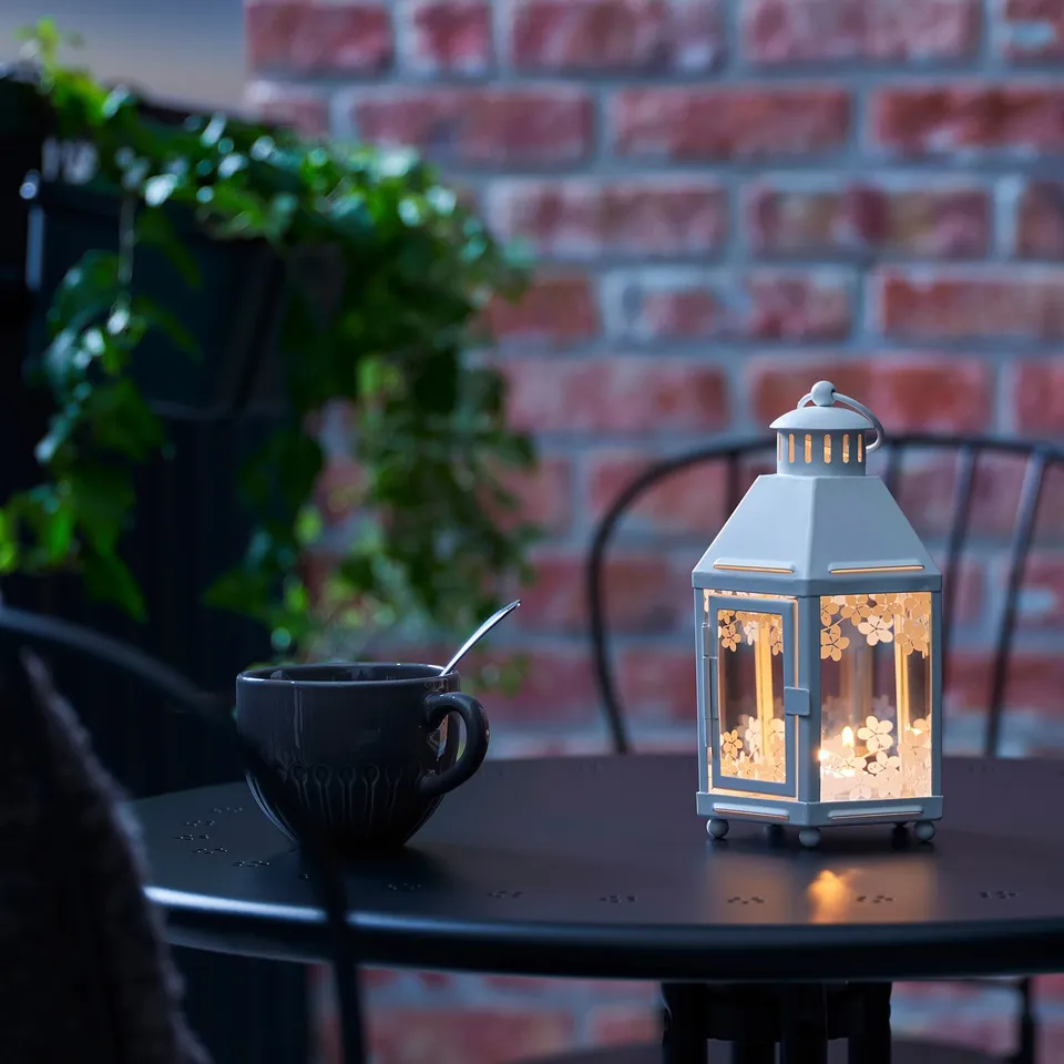 Cosy lantern with warm, glowing light sits on a table beside a mug and spoon. Ideal for creating a welcoming, romantic atmosphere.