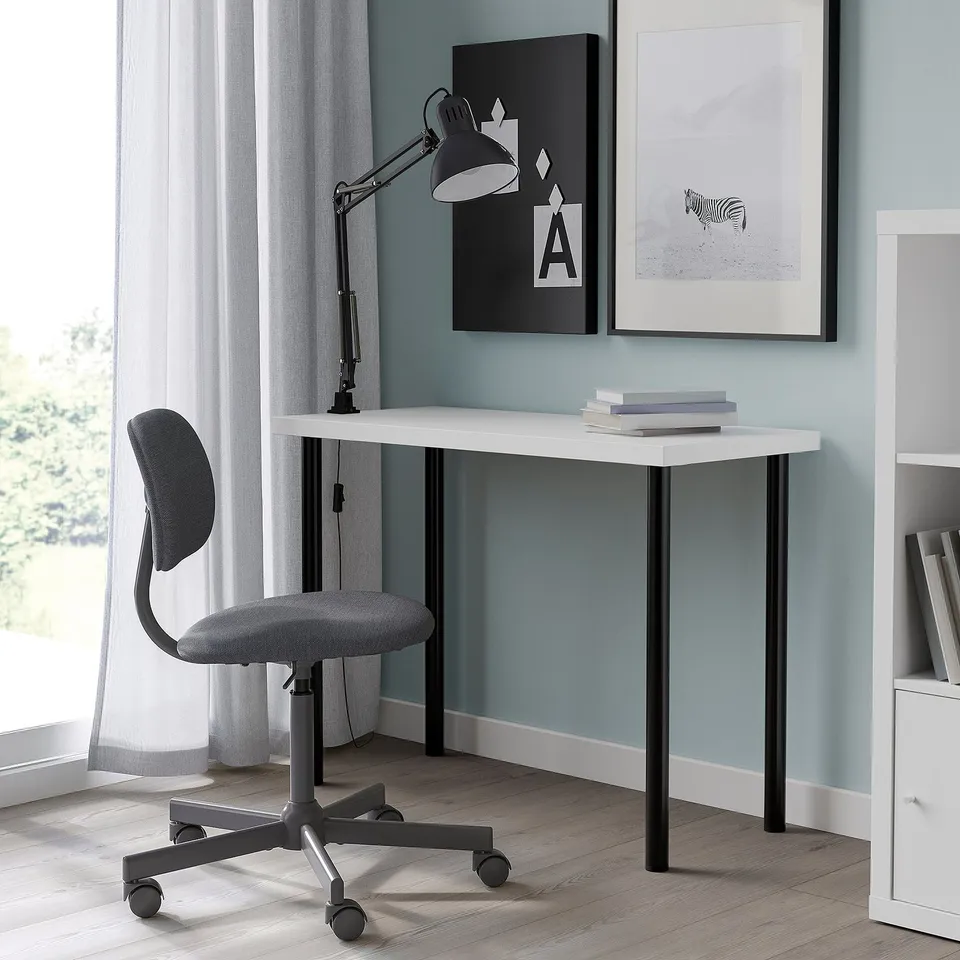 White LINNMON desk with black legs, grey office chair, black lamp. Small, fits in corner of light blue room. Two frames above. Minimalist setup.