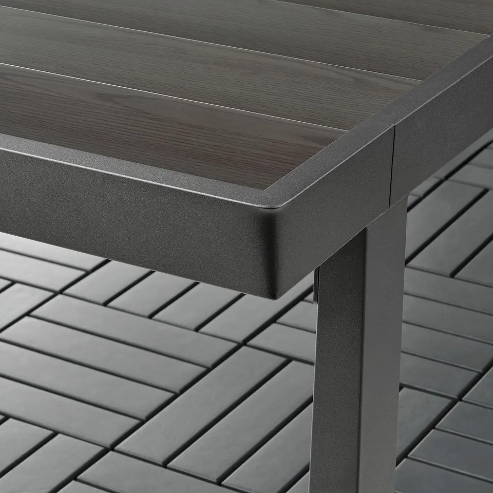 A modern, high-quality outdoor table with a dark, smooth metal surface and strong, slatted legs.