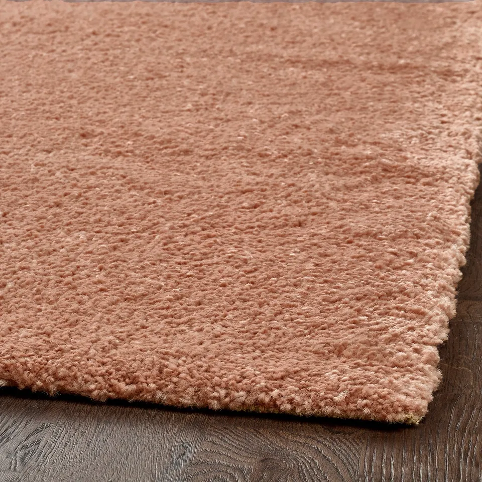 Soft, pale pink area rug on wooden floor, textured, low pile.