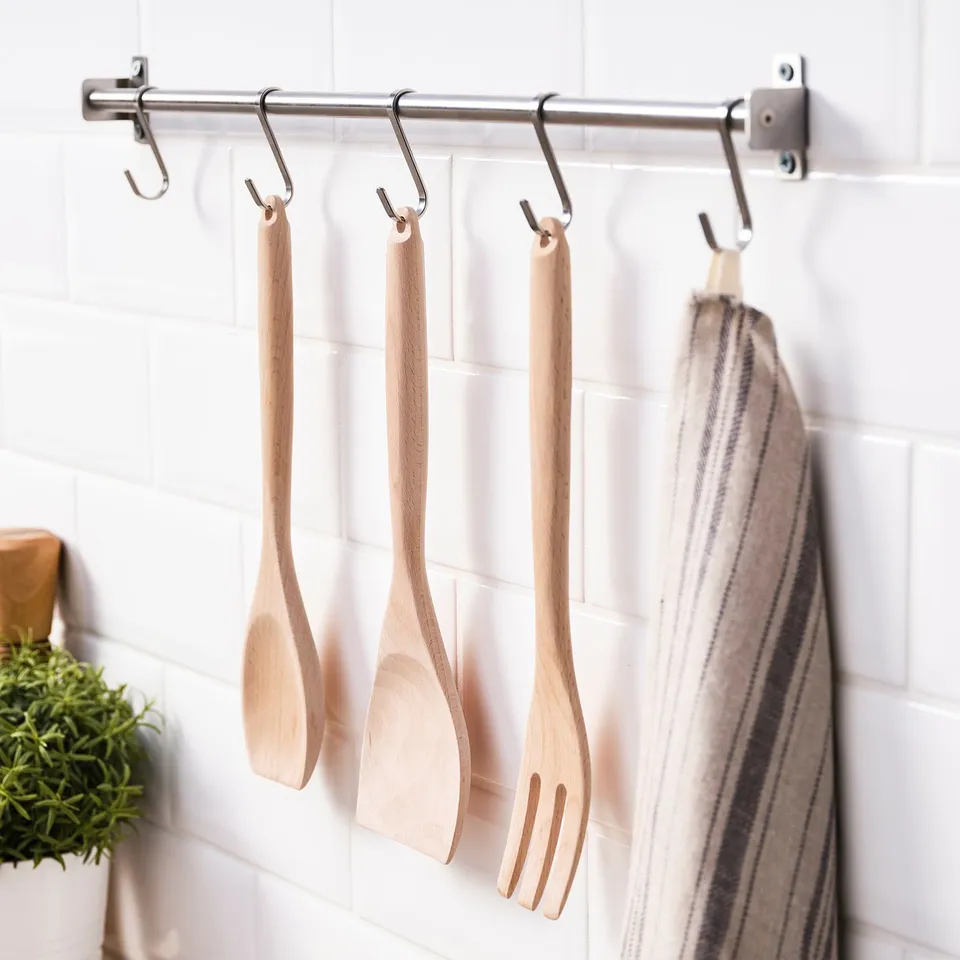 Wooden utensils hang from stainless hooks on white tiles.