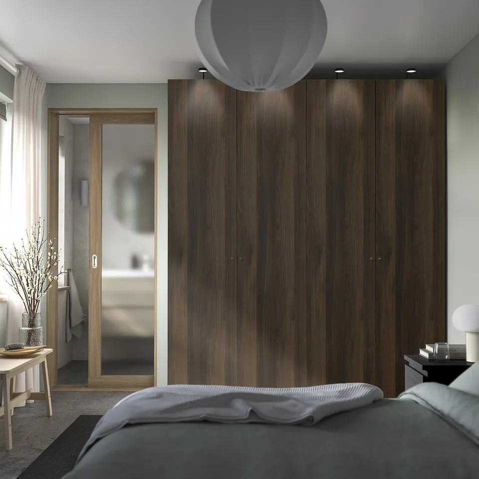 Modern bedroom with large PAX wardrobe in dark brown wood. Soft light, cosy bed, sleek decor.